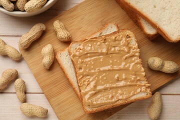 Delicious toasts with peanut butter and nuts on light wooden table, flat lay