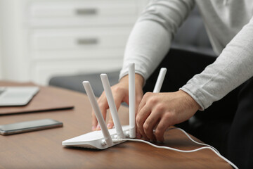 Man inserting cable into Wi-Fi router at wooden table indoors, closeup
