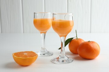 Tasty tangerine liqueur in glasses and fresh citrus fruits on white table