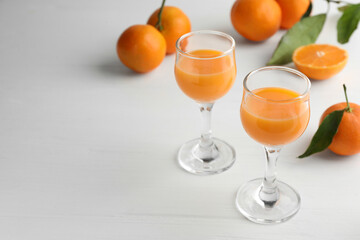Tasty tangerine liqueur in glasses and fresh fruits on white table. Space for text