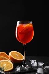 Glass of tasty Aperol spritz cocktail with orange slices and ice cubes on table against black background