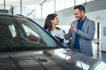 Portrait of a beautiful young couple choosing a new car at a car dealership. Buying a long-awaited car. Couple buying the car. Pair in a car salon. Husband with vife choose the automobile