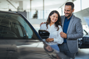 Cute couple peering into a car at a dealer while deciding whether to buy. Spouses Looking At Car...
