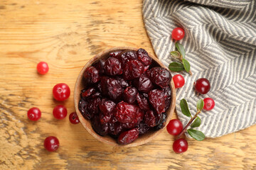 Tasty dried cranberries in bowl, fresh ones and leaves on wooden table, top view