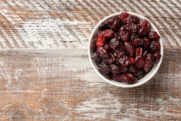 Tasty dried cranberries in bowl on rustic wooden table, top view. Space for text