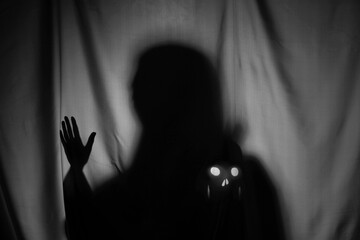 Silhouette of creepy ghost with skull behind grey cloth