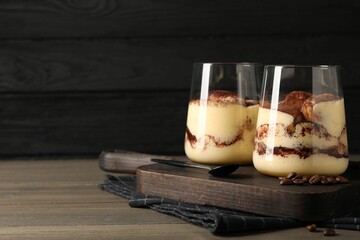 Delicious tiramisu in glasses, spoon and coffee beans on wooden table. Space for text