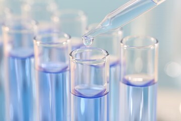 Laboratory analysis. Dripping light blue liquid from pipette into glass test tube on blurred background, closeup