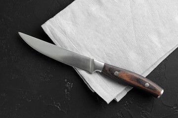 One sharp knife and napkin on dark textured table, top view