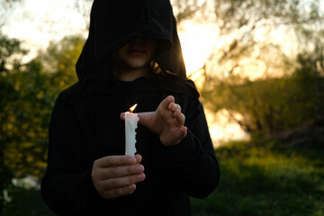 dress black witch with burning candle in hand, dark abstract forest background. sign of protection,...