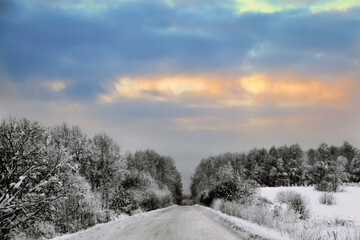 Beautiful sunrise behind clouds over a snowy country road.