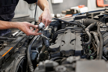 Fototapeta na wymiar Close-up of a worker, a repairman, repairing a car. The open hood of the car in the repair garage.