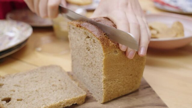 Cutting a slice of bread using a sharp breadknife at the dinner table.