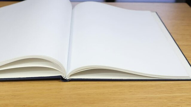 Hand open notebook with blank page on wooden background Focus on first floor.