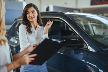 Car dealership manager helps a client choose a car. Female sales manager selling electric car to a female customer at showroom. Beautiful caucasian female client customer choosing new car.