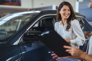 Professional manager shows and taking about car to female client in dealership. Happy salesman...
