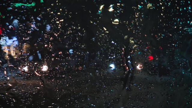 Winter night urban traffic scene as seen through the vehicle window covered with sleet drops. Melting snow water drips on the car windshield