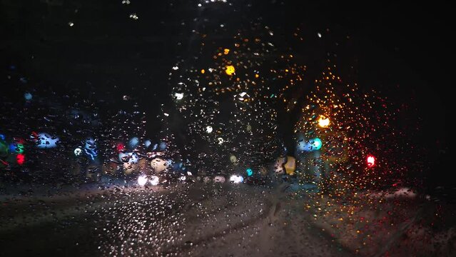 Winter night urban traffic scene as seen through the vehicle window covered with sleet drops. Melting snow water drips on the car windshield