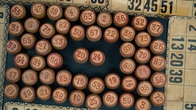 Cinematic close-up smooth shot from above of a pile of Bingo wooden barrels in a square, woody figures, old numbers background, vintage board game, slow motion 120 FPS commercial video pan right