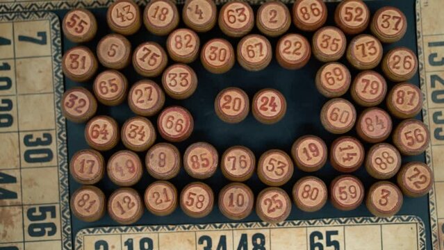 Cinematic close-up smooth shot from above of a pile of Bingo wooden barrels in a square, woody figures, old numbers background, vintage board game, slow motion 120 FPS commercial gimbal tilt up