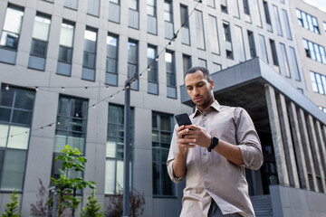 A man stands in front of a building, engrossed in his cell phone. Serious and thinking typing smartphone