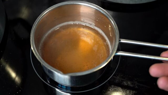 Person slowly swirls small pan of fresh, homemade bone broth heating on stove.