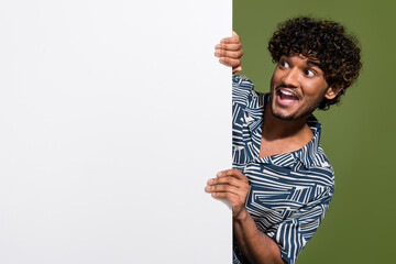 Photo of surprised indian man young subscriber hiding behind billboard looking at special price...