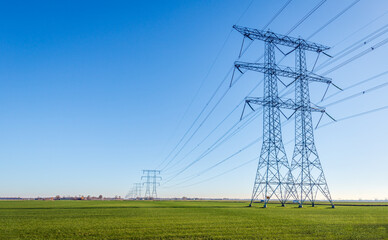 High-voltage pylons and lines contrasting against a blue sky. The masts are positioned on a vast...