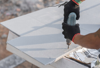 Hand worker installing white roof tiles and fix screw, Rooftop house construction site 