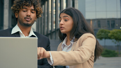 Indian businesswoman leader boss mentor dissatisfied talk to businessman showing mistake advice intern with laptop problem data business Arabian colleagues partners discuss project computer in city