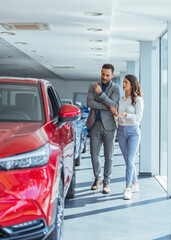 Young couple peering into a car at a dealer while deciding whether to buy it. Beautiful young...