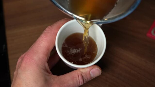 Person pouring hot bone broth from pan into mug, slow motion top down view.