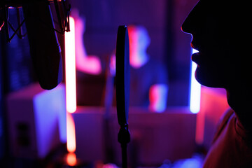 Young man enjoys singing a song in a modern recording studio. backlight, neon and smoke.