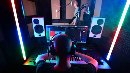 Young male singer in headphones singing in modern sound studio. Male sound engineer is working on a song.