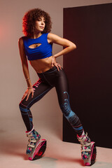 Sporty slim woman in leggings and top wearing kangoo jumper and posing in studio on background - 718041322