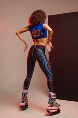 Beautiful sporty woman with curly hair in kangoo jumpers on studio background - 718041337