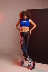 Beautiful sporty woman with curly hair in kangoo jumpers on studio background - 718041339