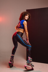 Beautiful sporty woman with curly hair in kangoo jumpers on studio background - 718041354