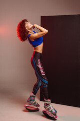 Beautiful sporty woman with curly hair in kangoo jumpers on studio background - 718041360