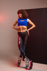 Beautiful sporty woman with curly hair in kangoo jumpers on studio background - 718041379