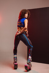 Sporty slim woman in leggings and top wearing kangoo jumper and posing in studio on background - 718041380