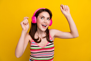 Obraz na płótnie Canvas Photo of lovely girl dressed striped top dancing in headphones look at promo empty space isolated on bright yellow color background