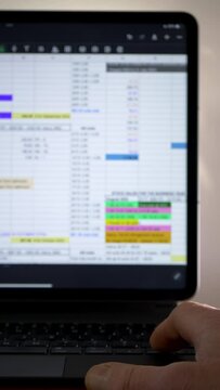Vertical video social media format &ndash; Closeup of a hand using a laptop or tablet keyboard to scroll through data in a spreadsheet app on a screen display.