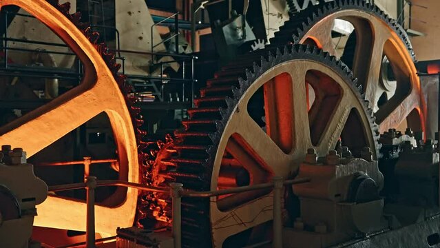 Big industrial group of gears working in the machinery. Heavy-duty factory cogs slowly rotating. Wide shot.