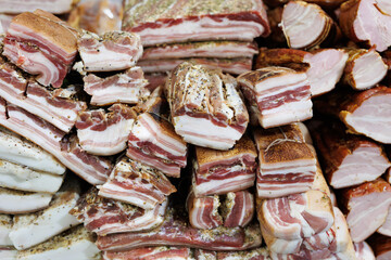 Large chunks of fresh salted bacon on the counter in the village market. The fibrous texture of the bacon and spices is clearly visible. Natural food.
