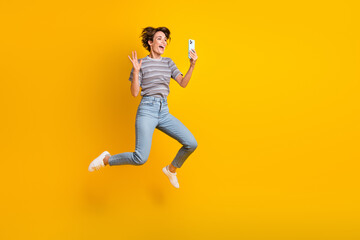 Full body photo of overjoyed energetic lady jump hold smart phone make selfie waving hi empty space...