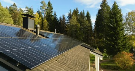 Drone flying backwards over sunlit photovoltaic panels on a house roof, fall day