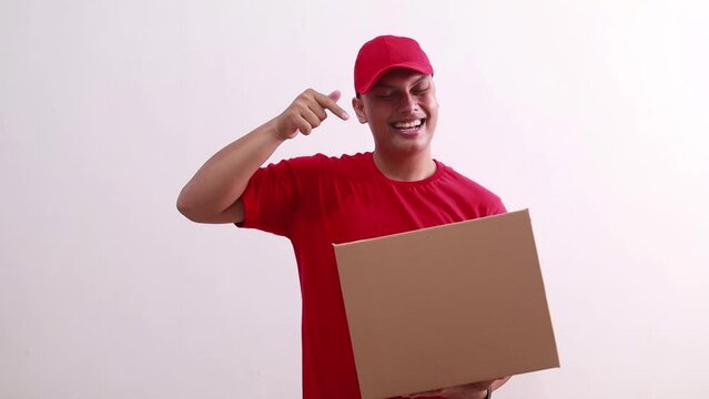 Happy young asian courier man holding cardboard while pointing on it. Isolated on white