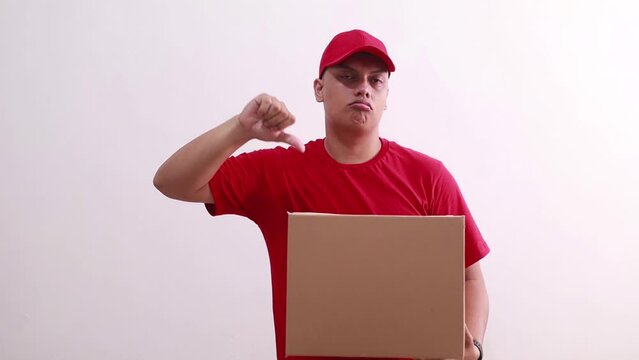 Young asian courier man holding a cardboard while showing thumbs down. Unsatisfied concept