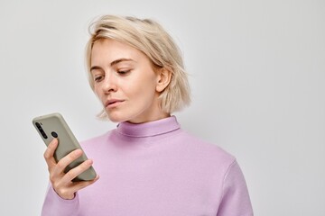 Fototapeta premium Portrait of young blond woman holding mobile phone in hand with happy smiling face. Person with smartphone isolated on white background.